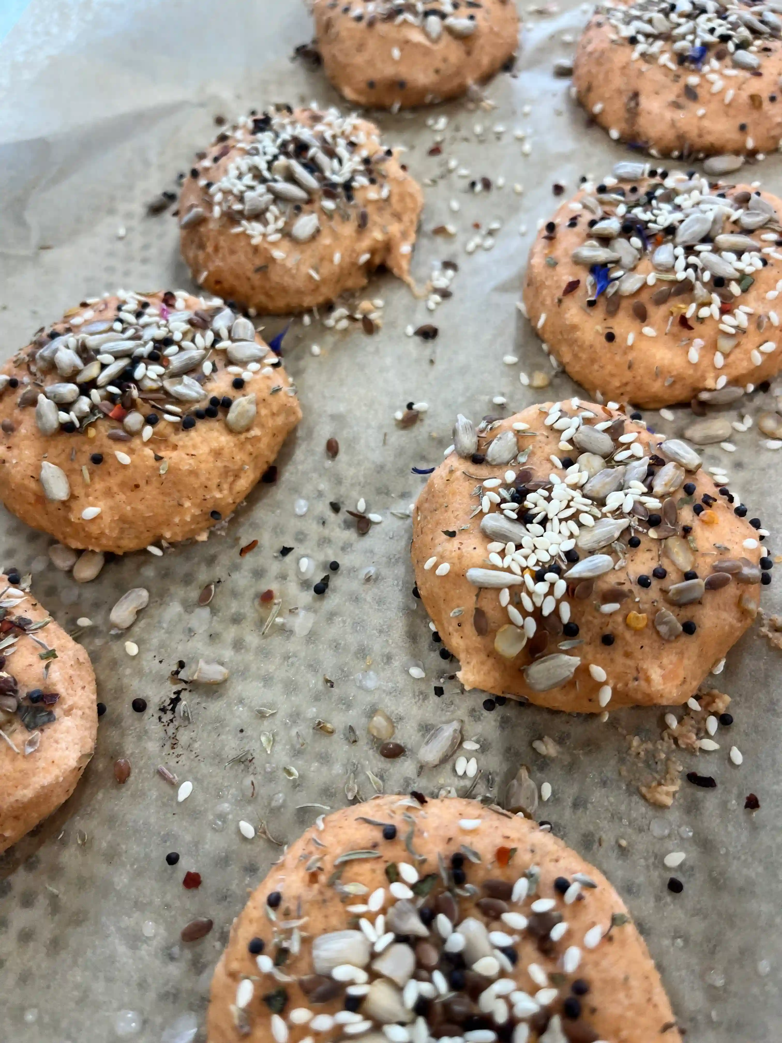 Unbaked savory biscuits topped with mixed seeds on parchment paper.